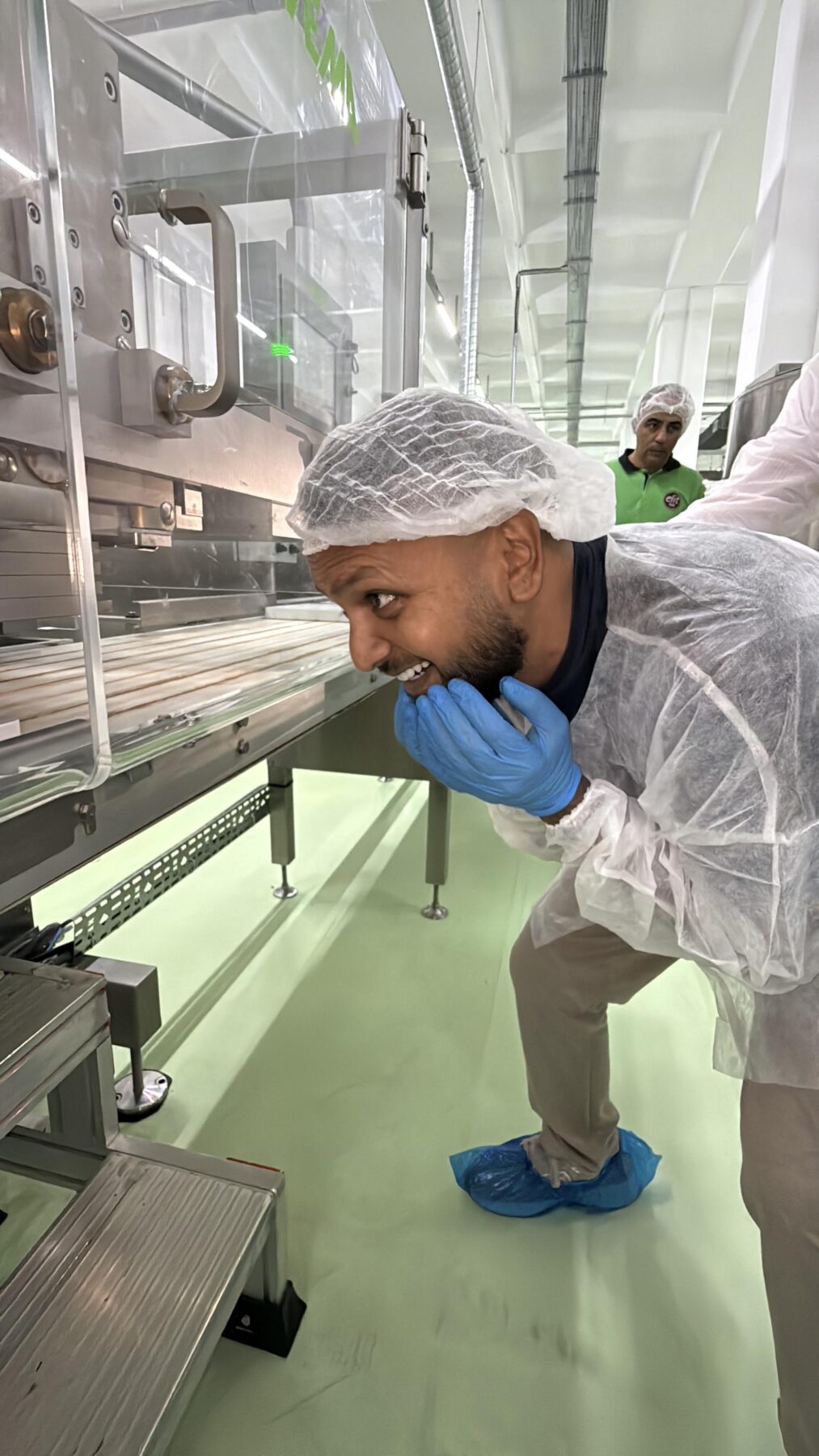 Cha Chi Versaci kijkt met een grote glimlach over de productielijn waar de repen voorbijkomen.